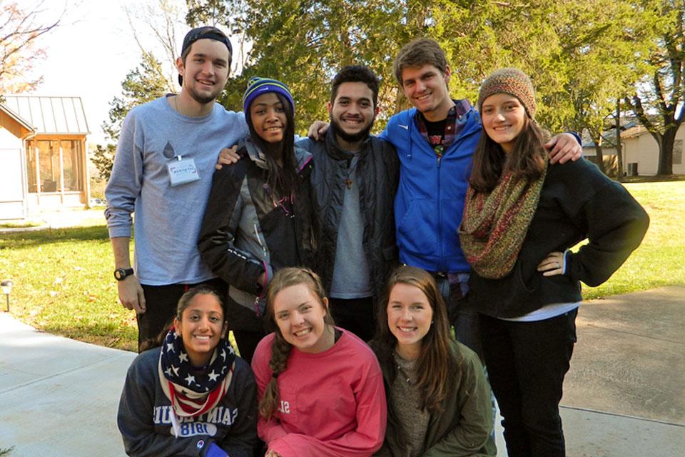 A group of 8 students pose for a photo outdoors while preparing for a retreat.