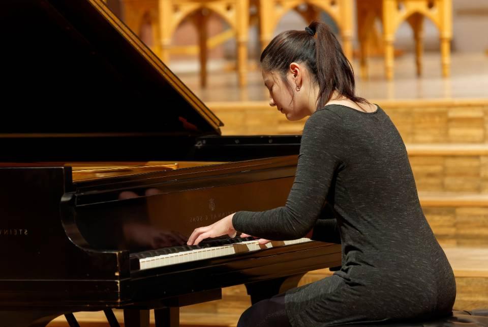 A student plays a grand piano during a concert.