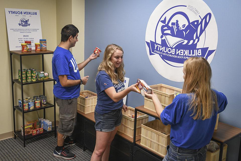 三个学生在捐赠物品的篮子和货架中检查食品包装.