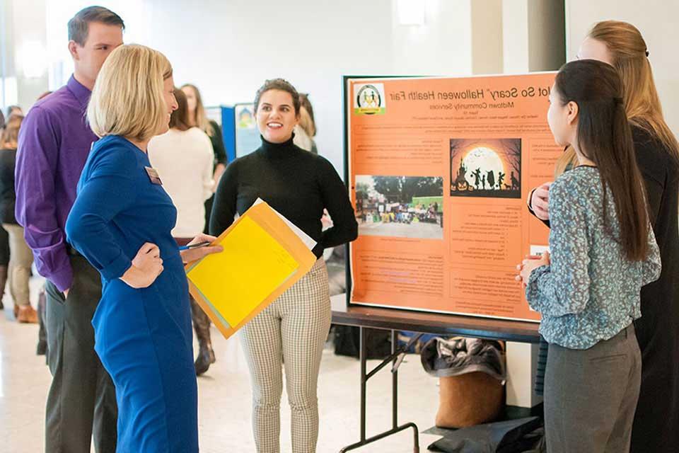 A group of college students presents a posterboard with student research findings