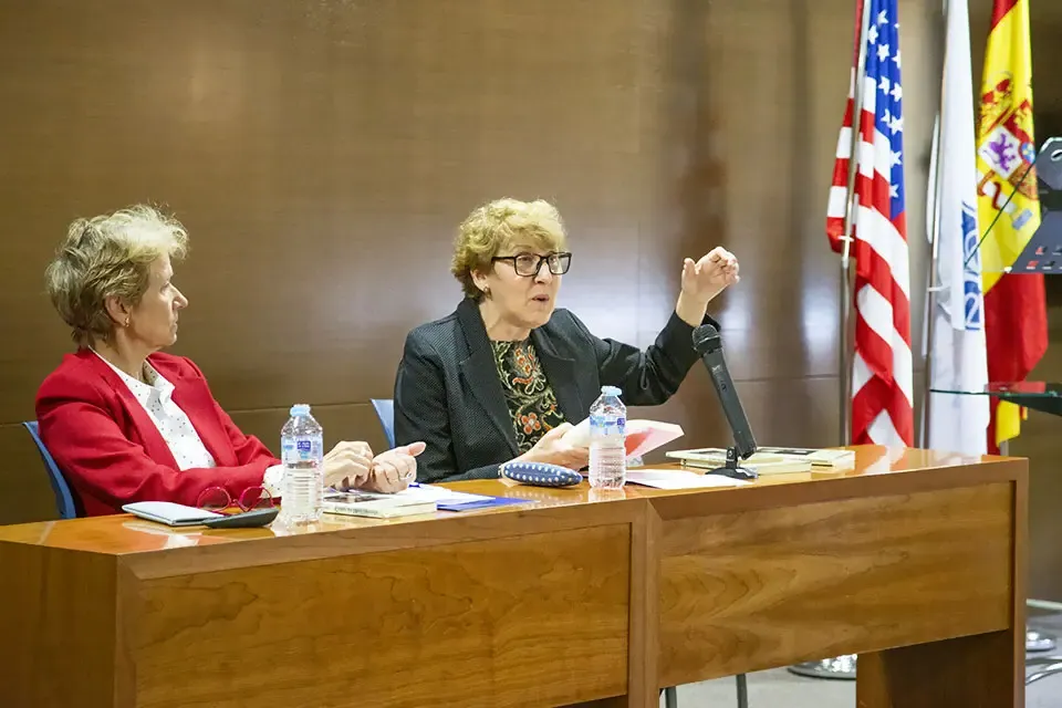 两个女人坐在桌子旁辩论，身后有三面旗帜
