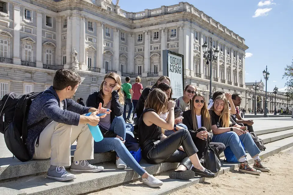 Students sit on steps outside a large white building with columns.