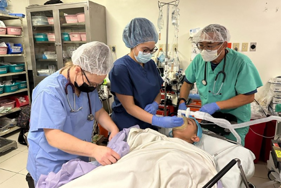 三个穿着手术服的医生, and surgical protective equipment attend to a patient in a medical facility.