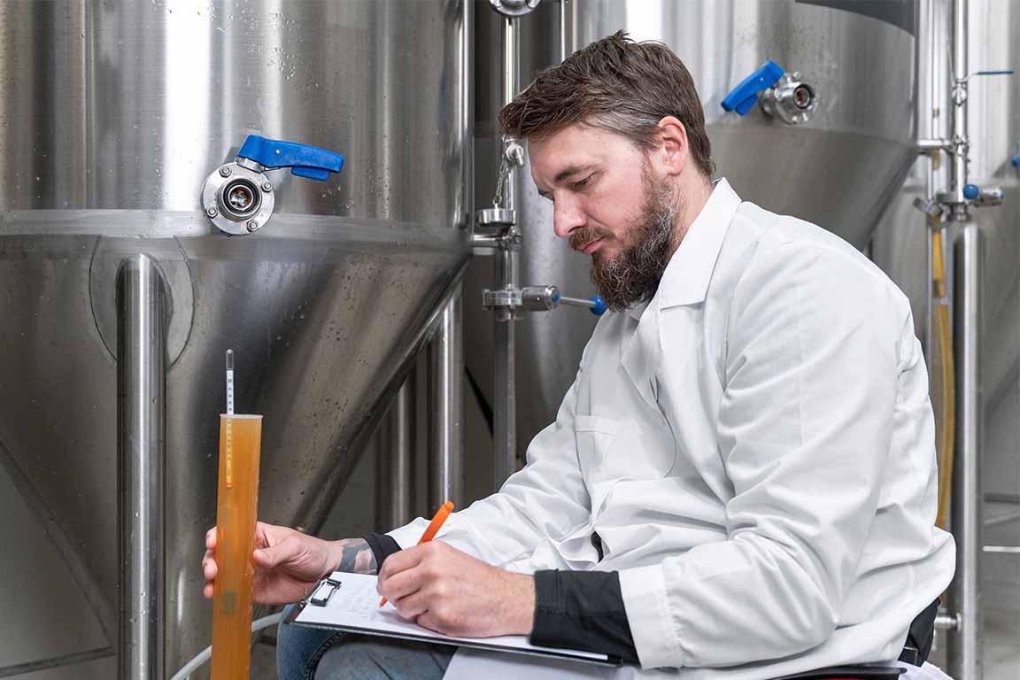 一个男人站在一罐啤酒前，在写字板上写字