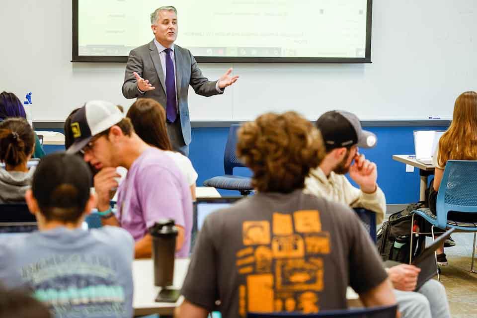 A male professor lectures in front of a full classroom
