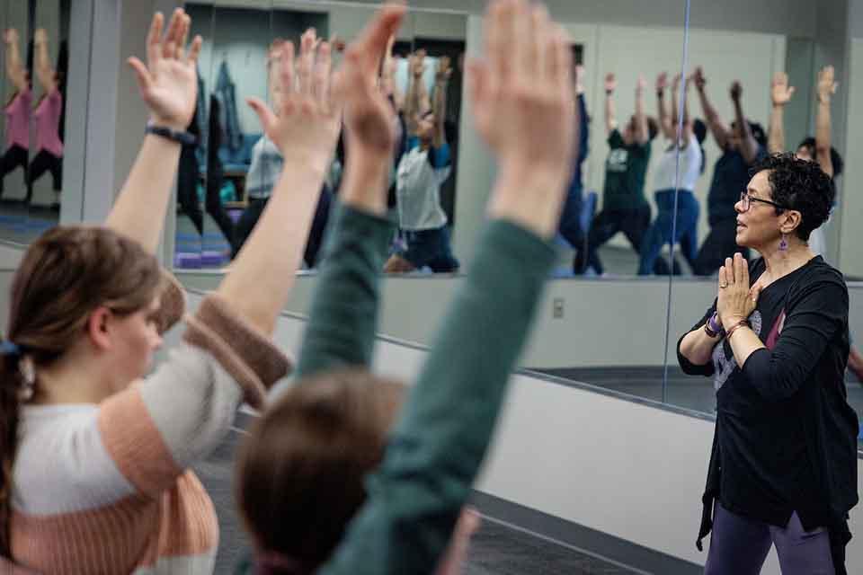 A teacher leading a yoga class in front of a mirror with students facing her