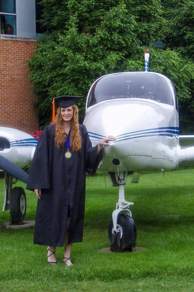 苏利文穿着毕业礼服站在帕克斯大厅前的飞机旁.